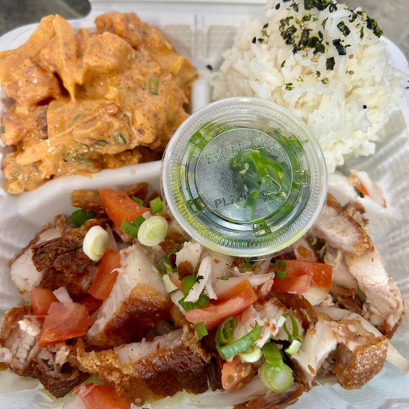 A takeout container with crispy pork belly, spicy tuna poke, rice, and a side of seaweed salad.